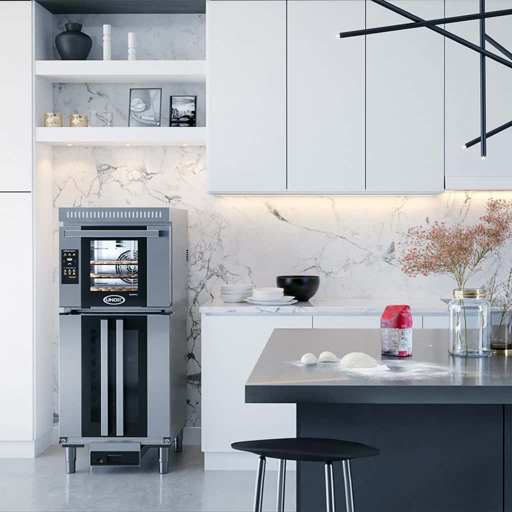 Modern white home kitchen, an Unox oven on top of a prover sits next to the kitchen counter, dough and flour are on the kitchen table.