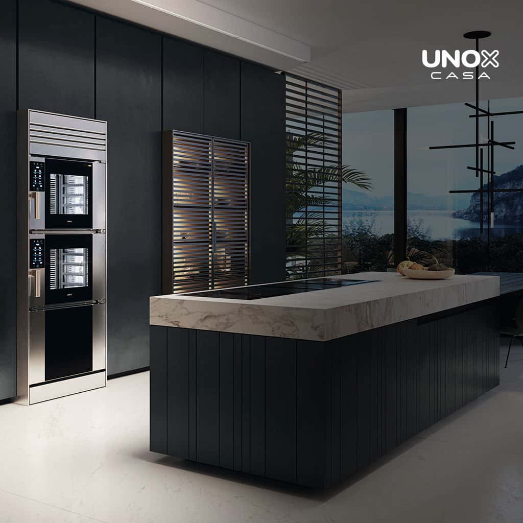 Cucina di lusso con grande piano in marmo e vista sull’oceano dalla finestra, con forno combinato a incasso, impilato su un altro.