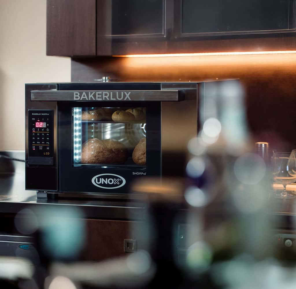 Horno de convección profesional de Unox horneando pan colocado sobre la encimera de un bar o una cafetería