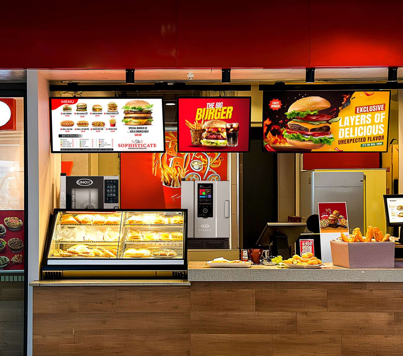The counter of a fast food restaurant with food on display, menu boards, a cash register, and Unox small commercial ovens in the background