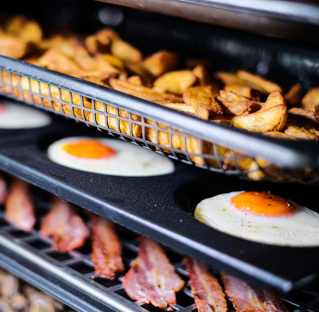 non-stick and micro-perforated aluminium Commercial baking trays inside a cooking chamber with potatoes, eggs, bacon and mushrooms on top