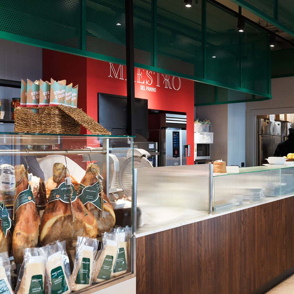 A deli counter with hams and cheeses behind, an Unox speed oven sits on the counter in the background.