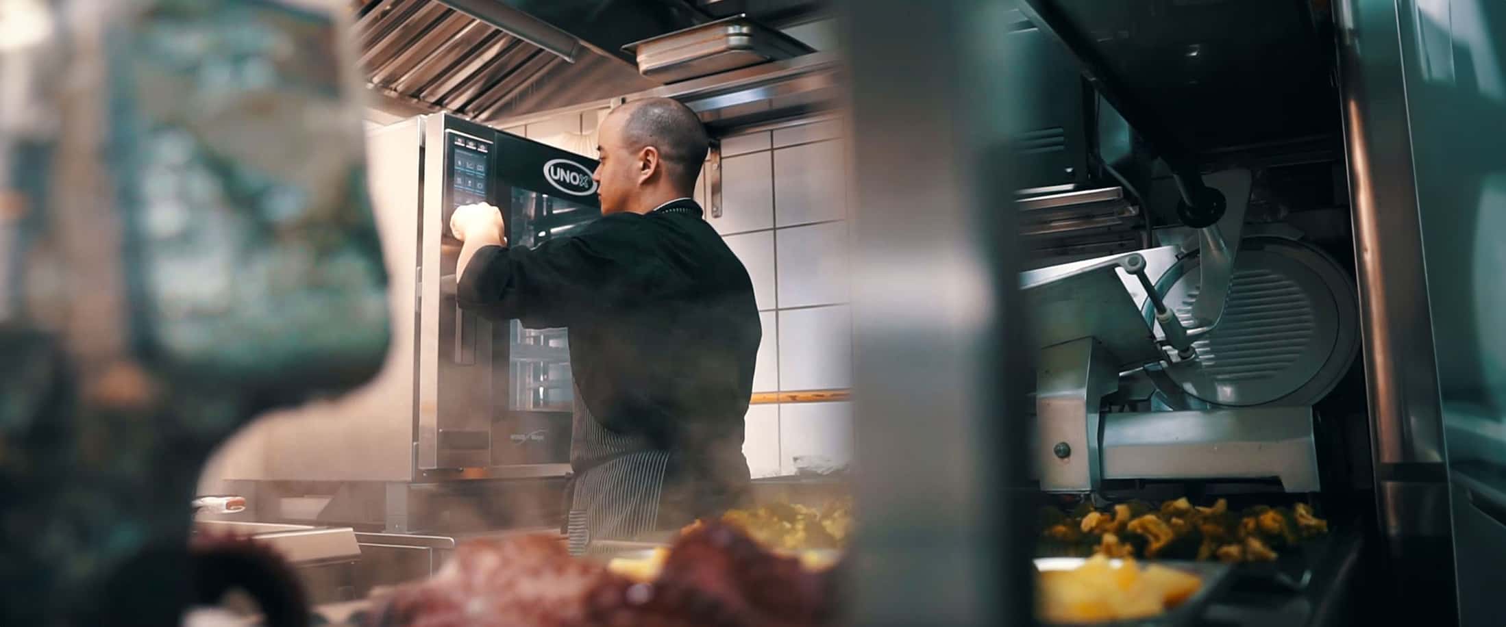 Male chef in kitchen pressing buttons on display of an Unox combi oven.