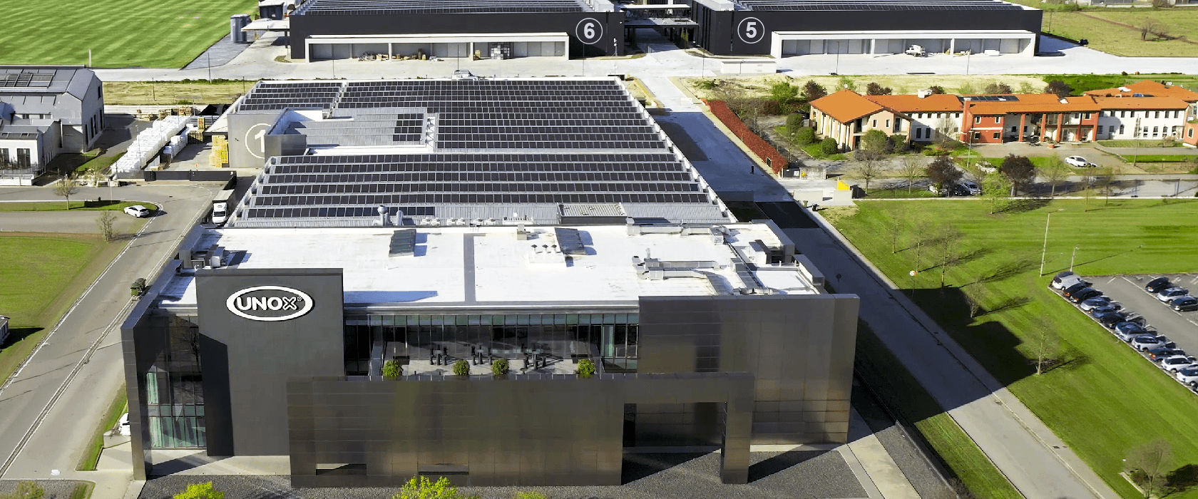 Overhead photo of field of solar panels amongst a block of buildings and surrounded by green fields.