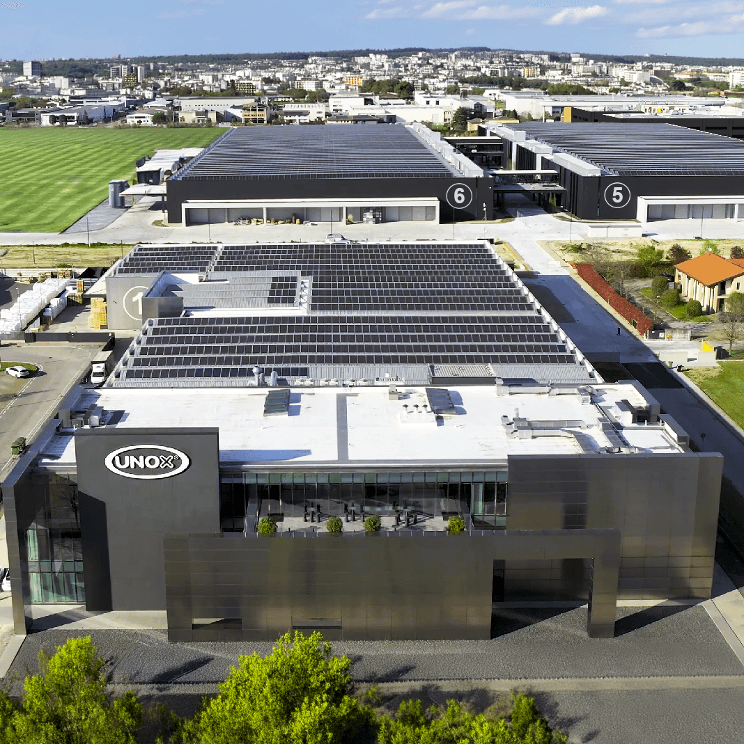 Overhead photo of field of solar panels amongst a block of buildings and surrounded by green fields.