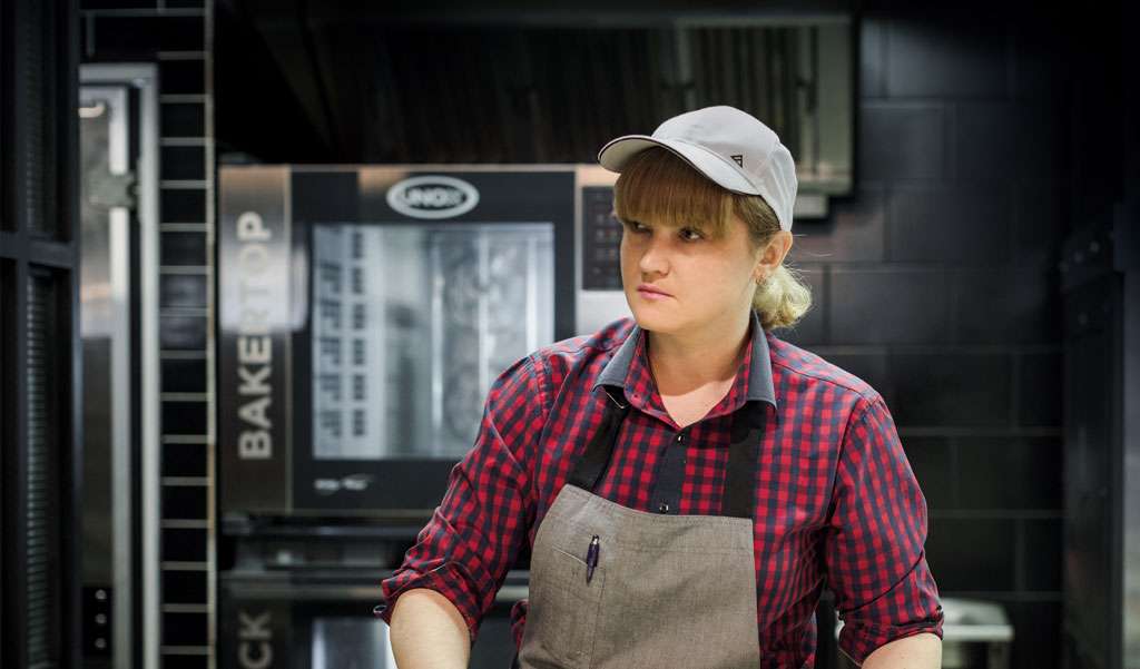 Operator working behind a bakery counter, with a cooking column composed of a Unox combi oven and a static oven below