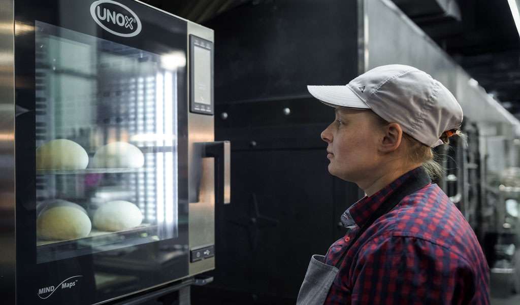 Operator working behind a bakery counter, with a cooking column composed of a Unox combi oven and a static oven below