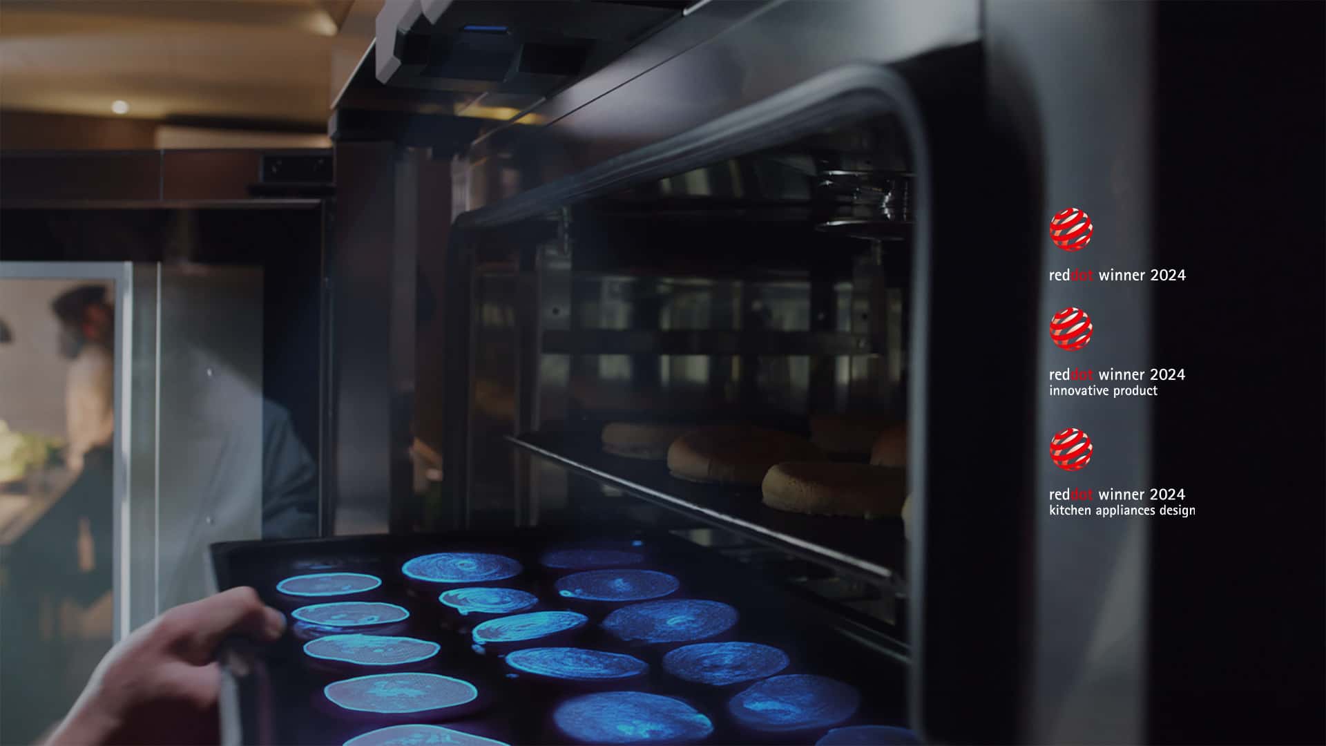 Una mano introduce una bandeja de comida en un horno Unox. Un sensor situado en la parte superior proyecta una luz azul sobre los alimentos para escanearlos e identificarlos.