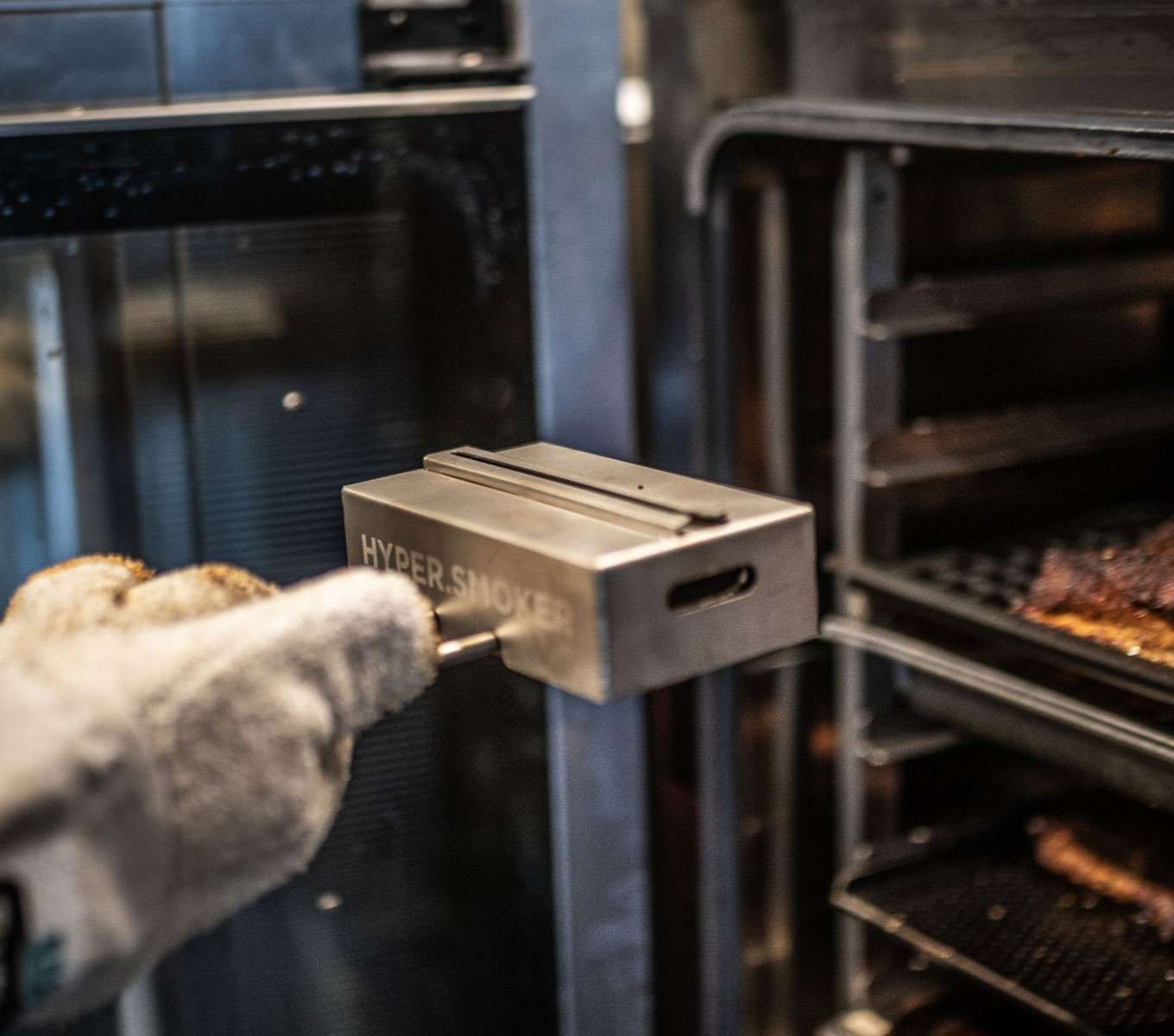 A gloved hand loading a Unox smoking accessory inside the cooking chamber of a commercial combi oven