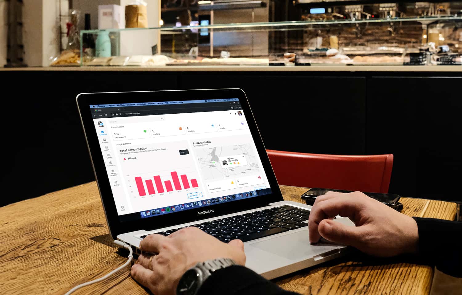 Man sat at table in café working on a laptop, graphs showing data can be seen on screen.