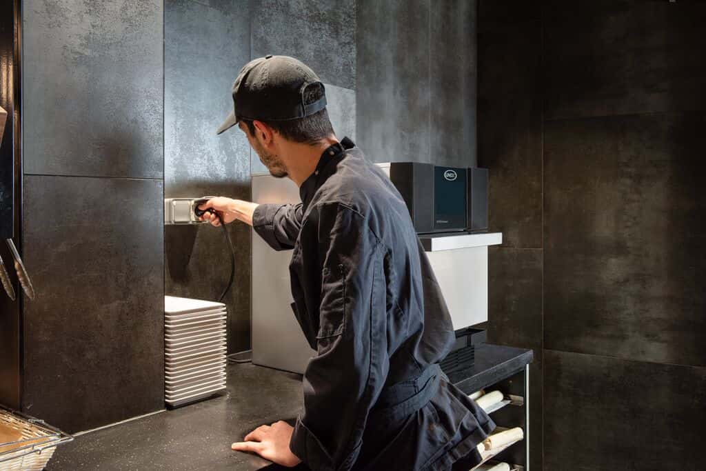 Un empleado de cafetería con camiseta negra enchufa fácilmente un horno Unox SPEED.Compact en el mostrador.