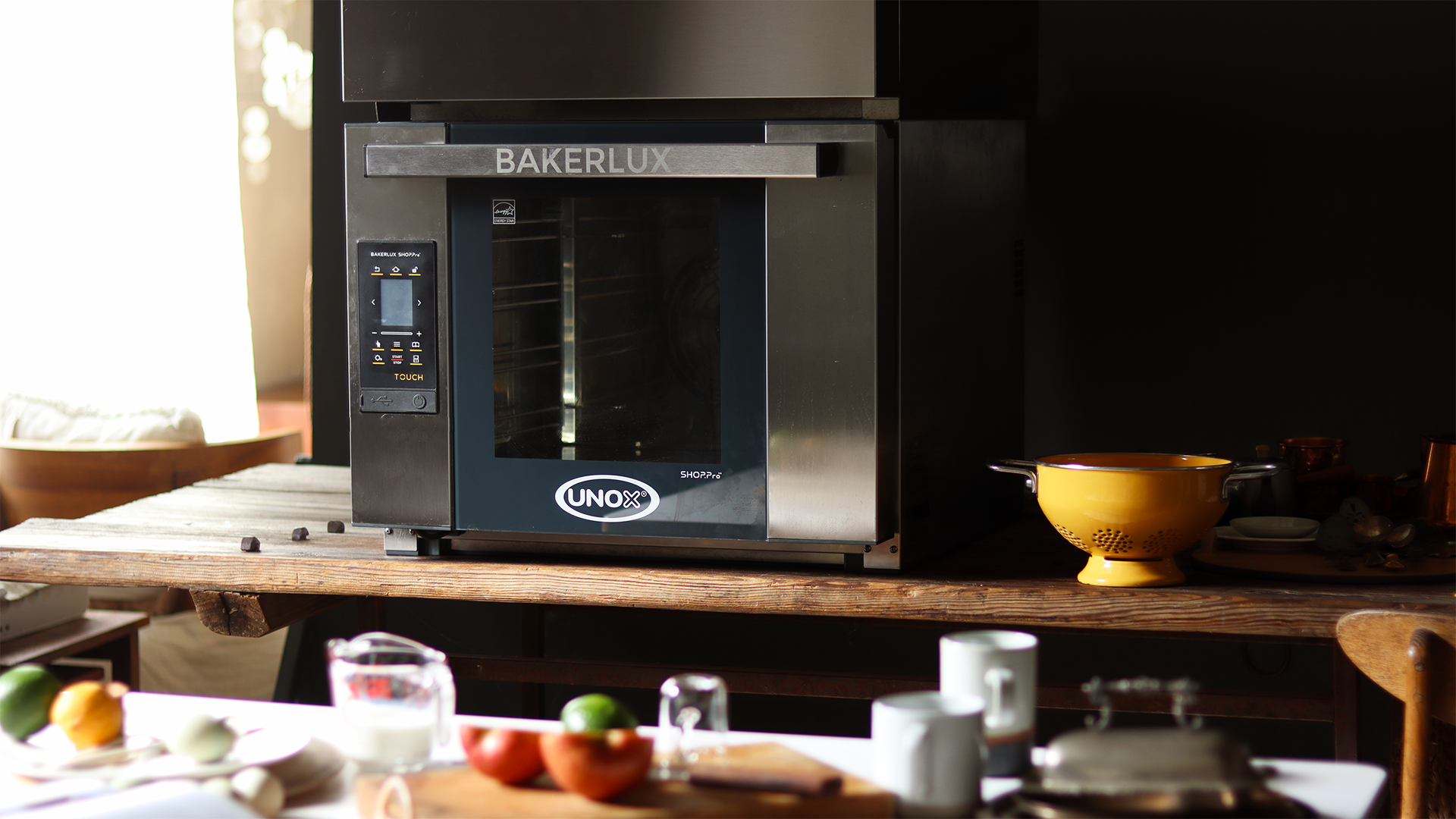Unox bakerlux oven sat on a wooden bench in a kitchen, fruits and vegetables in the foreground.