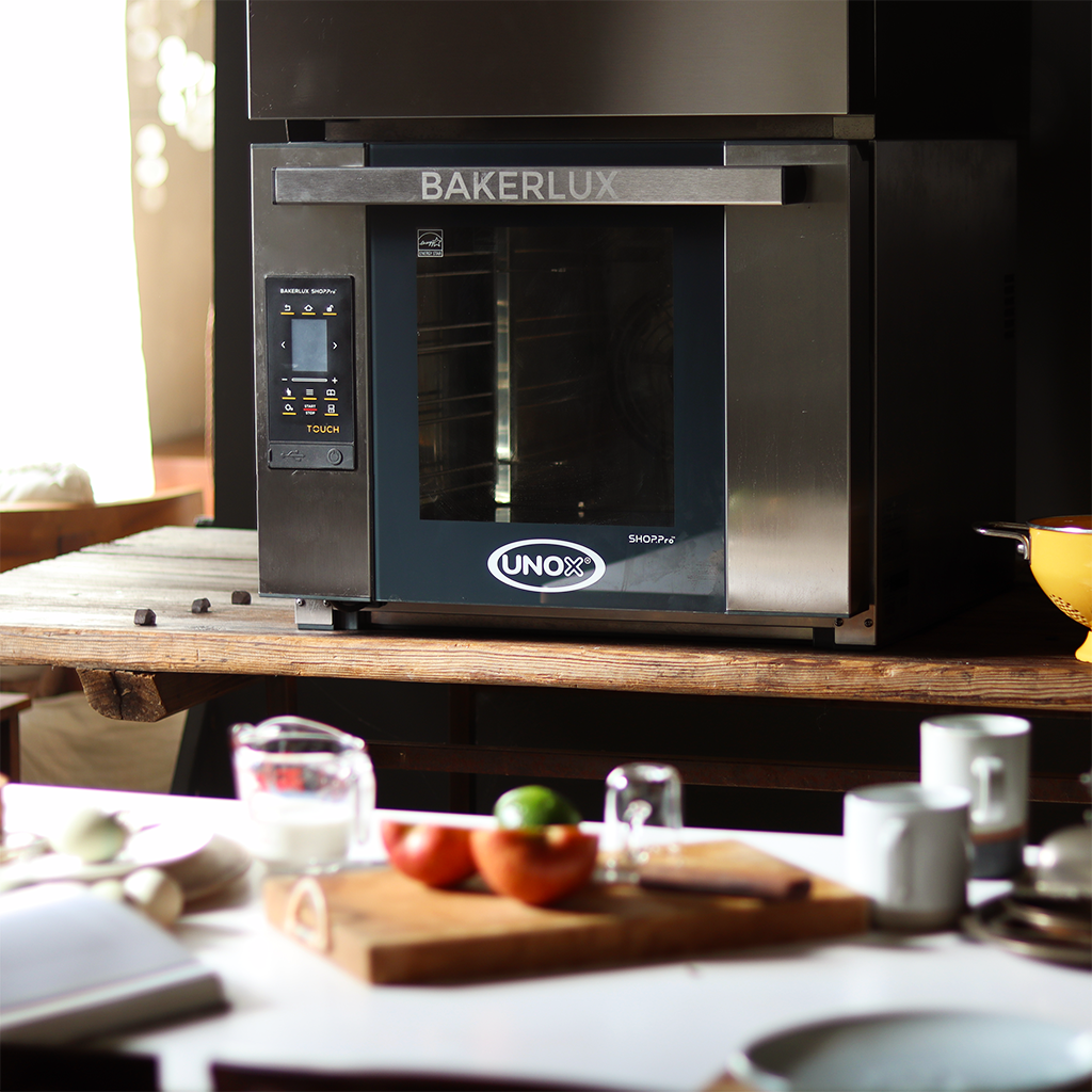 Unox bakerlux oven sat on a wooden bench in a kitchen, fruits and vegetables in the foreground.