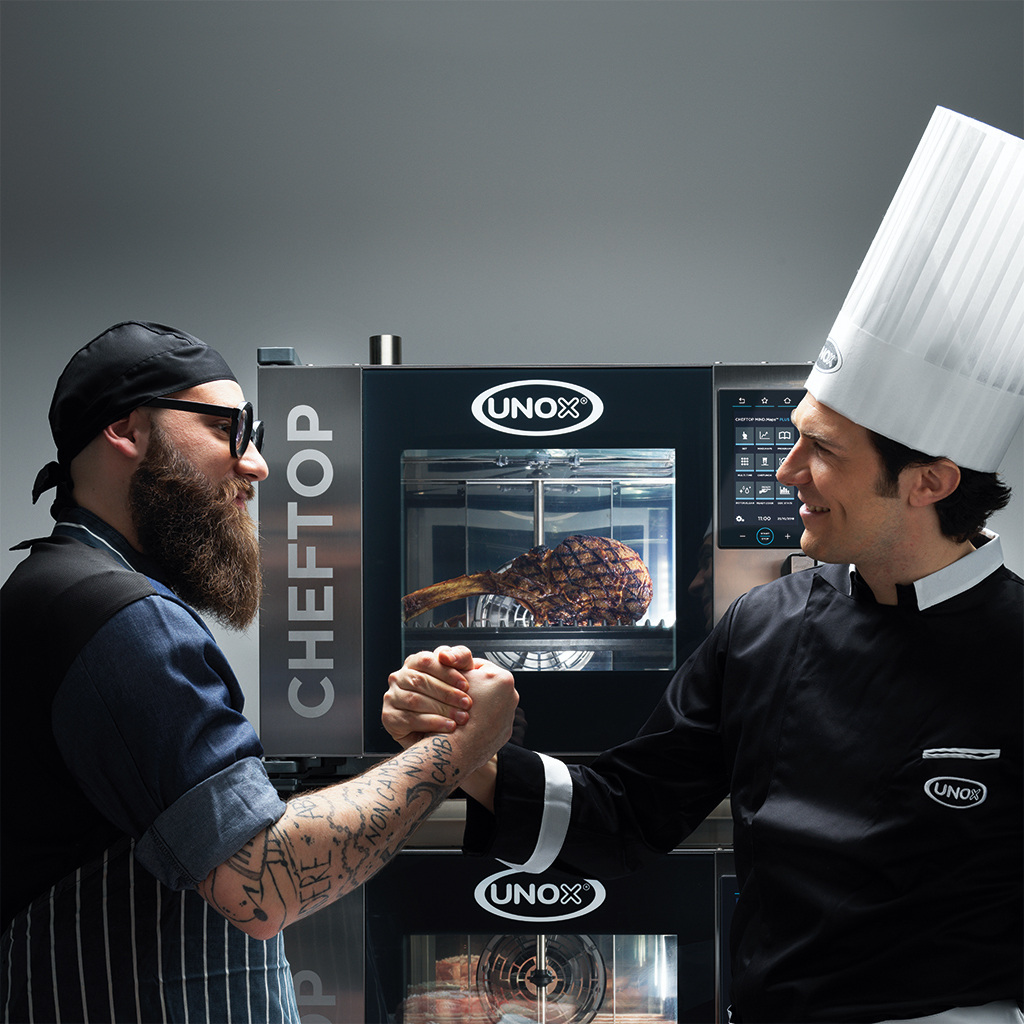 A male chef and a man wearing Unox uniform holding hands in front of an Unox combi oven.